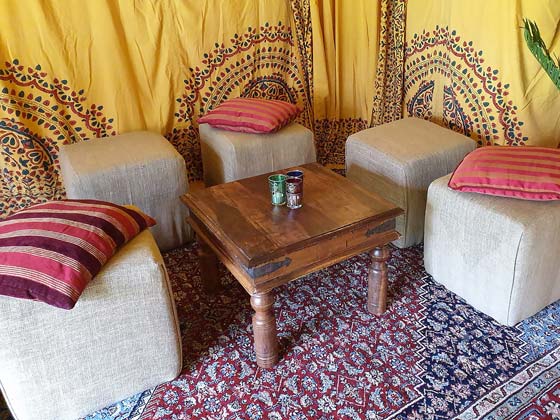 Hessian-Covered Cubed Pouffes with Scatter Cushions Around a Sheesham Table in a Bedouin Tent